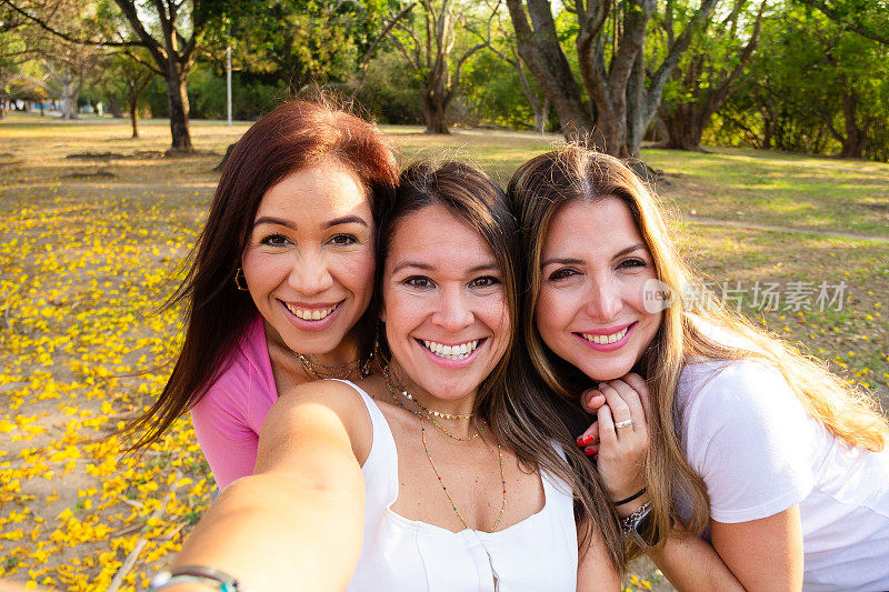 黄金时段，三位快乐微笑的成年女性朋友在户外公园自拍。友谊与幸福概念