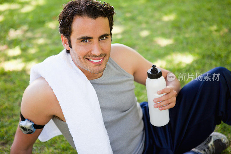 一个肩膀上搭着毛巾向上看的人，手里拿着一个运动瓶