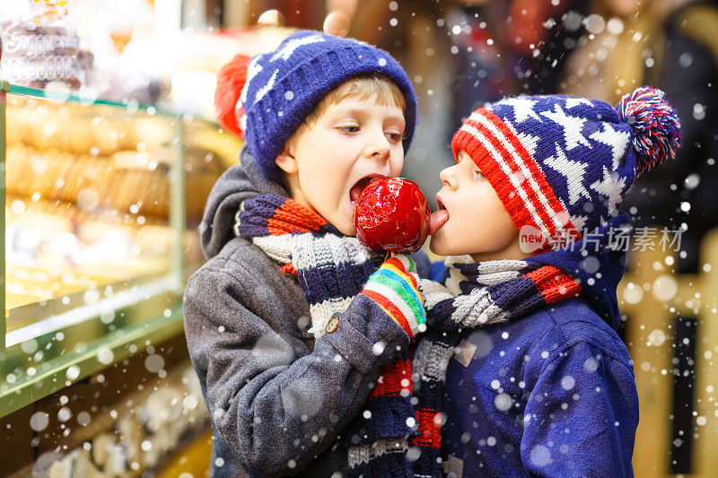 两个小男孩站在圣诞市场上吃着苹果糖