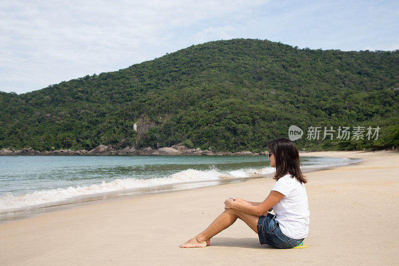一个美丽的女人坐在荒芜的海滩上望着大海。