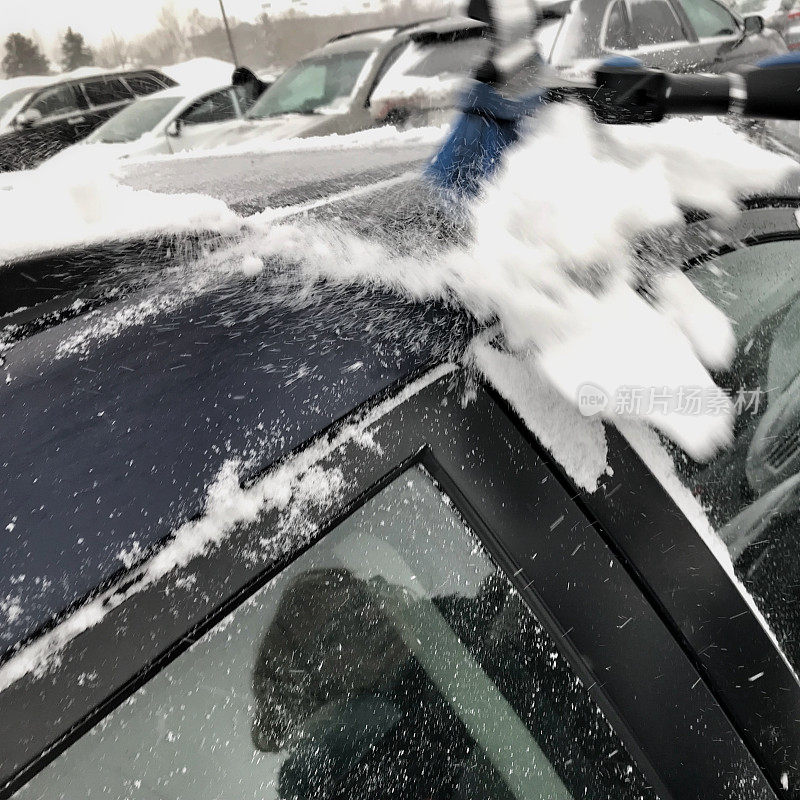 一位老妇人在一个下雪天清理她的车顶。