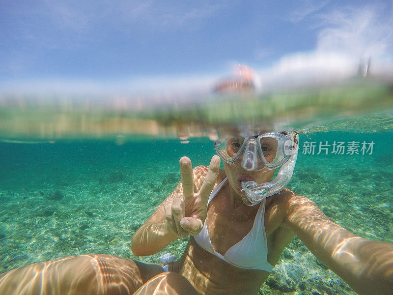 年轻女子在水晶蓝色的水下自拍，度假夏天的概念