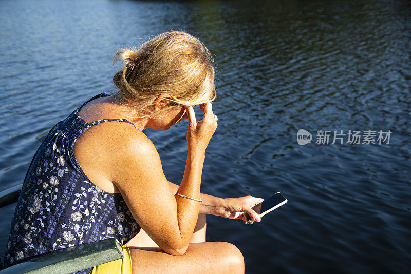 一个紧张或沮丧的女人在湖边用她的智能手机