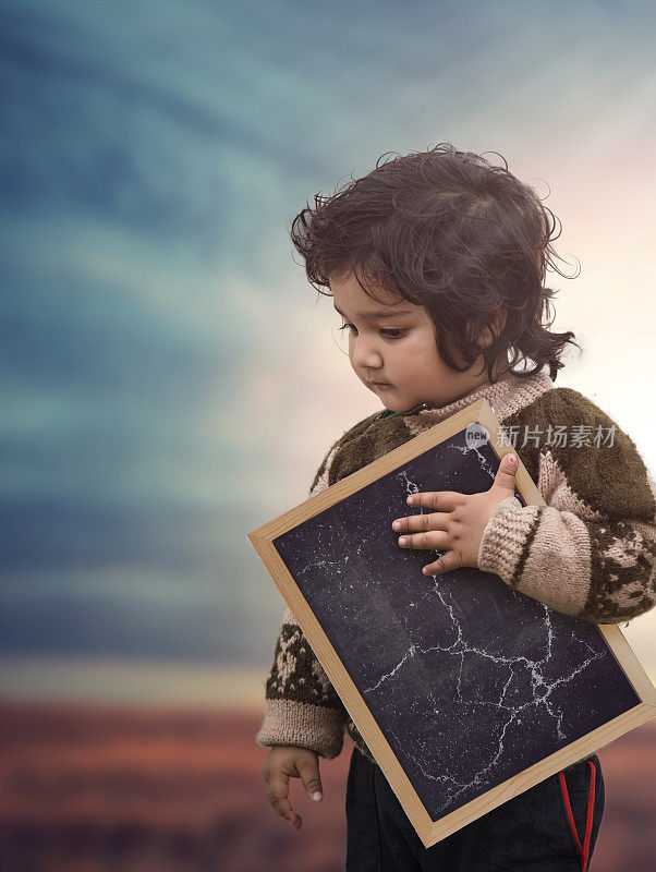 一个可怜的蹒跚学步的女孩的肖像拿着空白的黑板，儿童教育概念与复制空间。