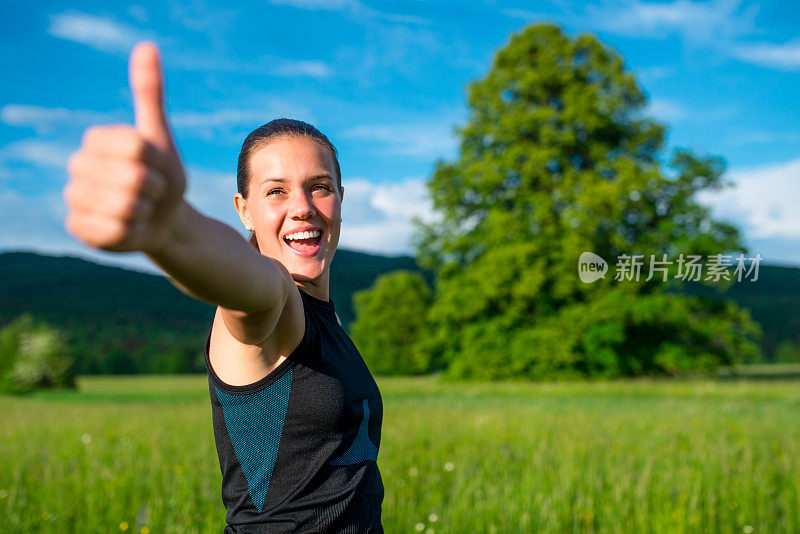 快乐的年轻女运动员在大自然中竖起大拇指