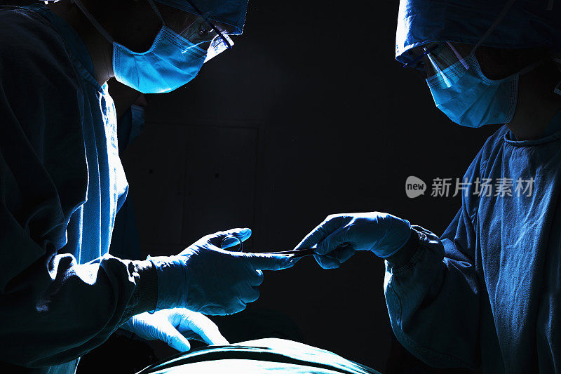 外科医生们在昏暗的手术室里通过手术设备