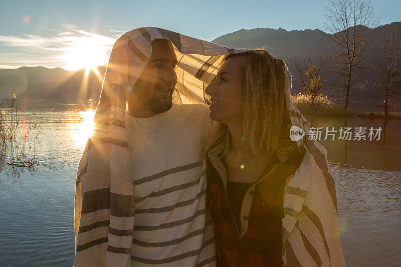 夕阳西下，湖边，一对快乐的年轻夫妇裹着毯子