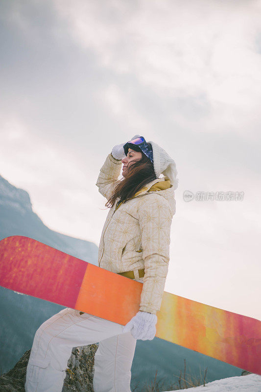 女人拿着滑雪板，背景是高山