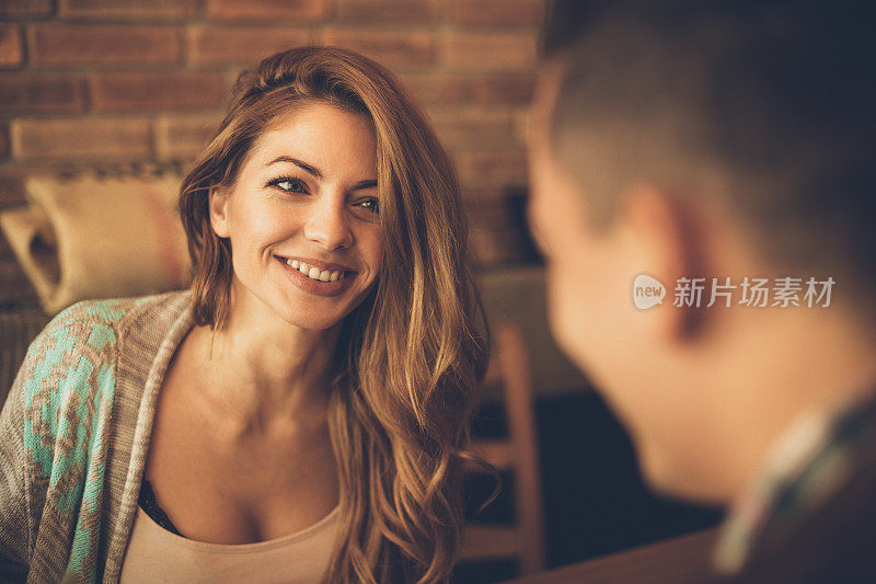 一个年轻的女人有一个大大的微笑，看着一个男人在一张桌子在咖啡馆