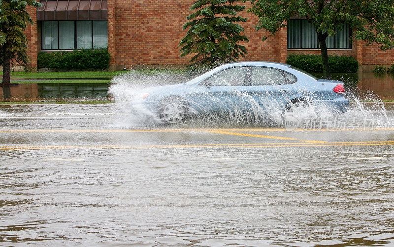 蓝色的汽车在被水淹没的街道上溅起水花