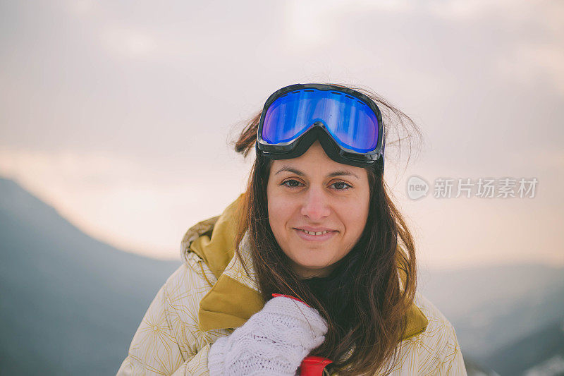 近景美丽的年轻女子在冬天的衣服站在一边，手拿木棍的背景雪山