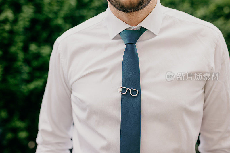 一个穿着白衬衫，打着蓝色领带，戴着别致的眼镜形状的领带夹的人