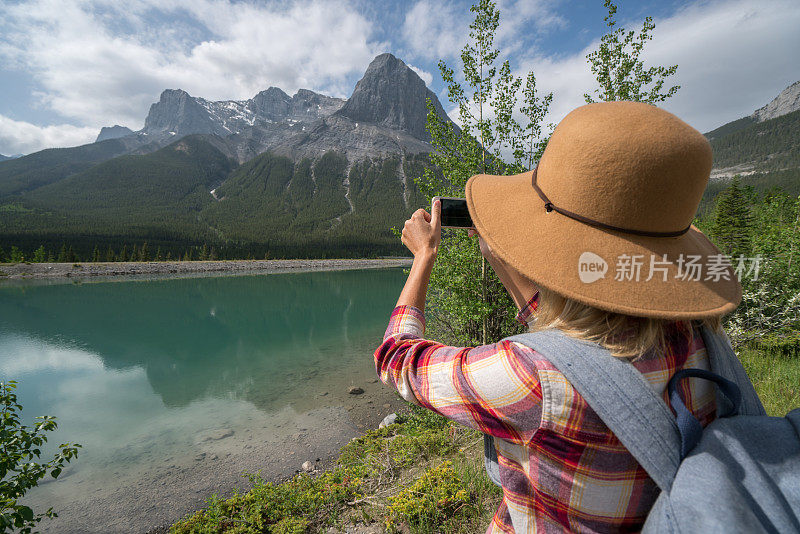 年轻女子徒步旅行者用智能手机拍照的山湖景观