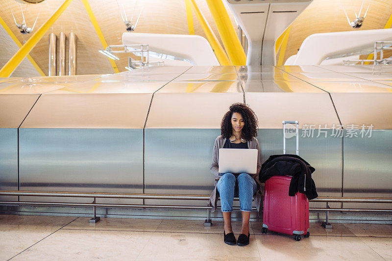 有魅力的黑人女性坐在机场，用笔记本电脑工作