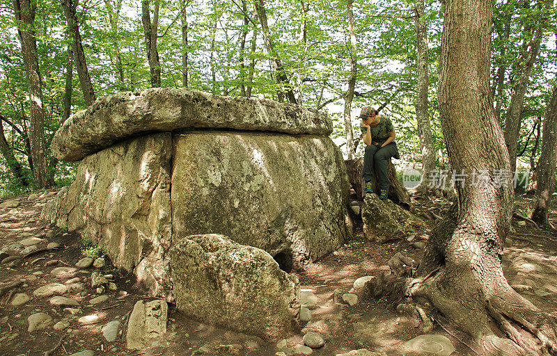 女旅行者坐在古代巨石石头人附近