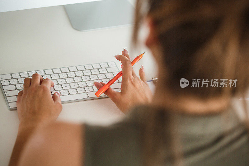 一个女人在办公桌旁拿着笔在键盘上打字
