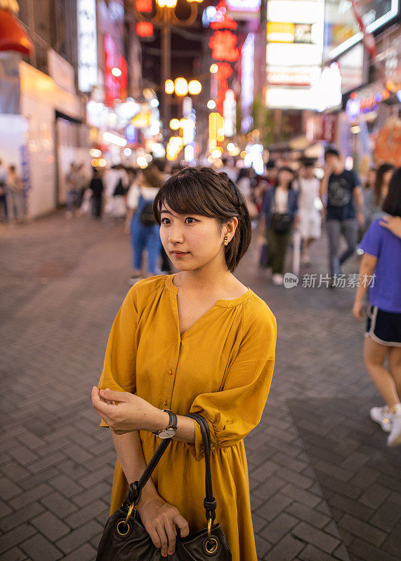 晚上，年轻女子站在日本大阪市中心的街道上