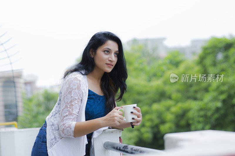 女人放松在阳台上拿着一杯咖啡或茶库存照片