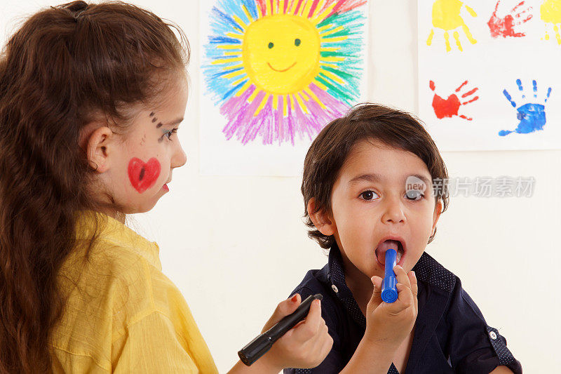 小女孩和小男孩正在画画。男孩把蜡笔放进嘴里。