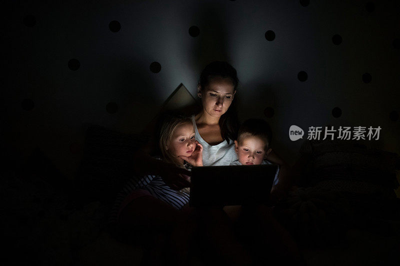 年轻的母亲与孩子坐在室内卧室，使用笔记本电脑。