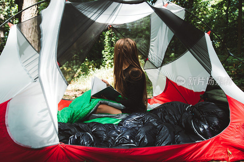 一个年轻女子在松林里的夏日日出时在帐篷里看书