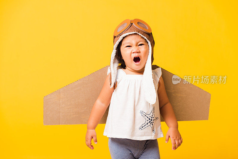 小孩小女孩微笑着戴着飞行员帽玩，护目镜和玩具纸板飞机机翼
