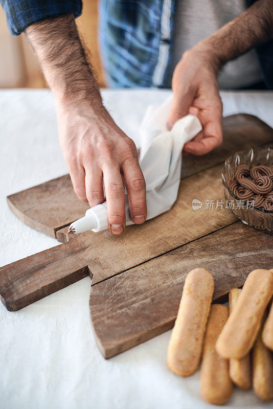 隔离烹饪:一名男子正在用糖衣袋给提拉米苏填馅