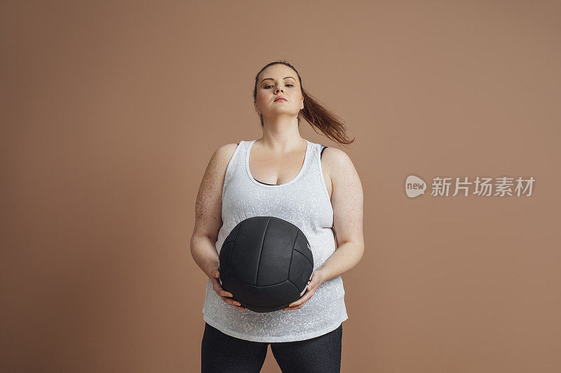 动机和决心:大尺寸的女人摆着一个药球，健身房的减肥概念