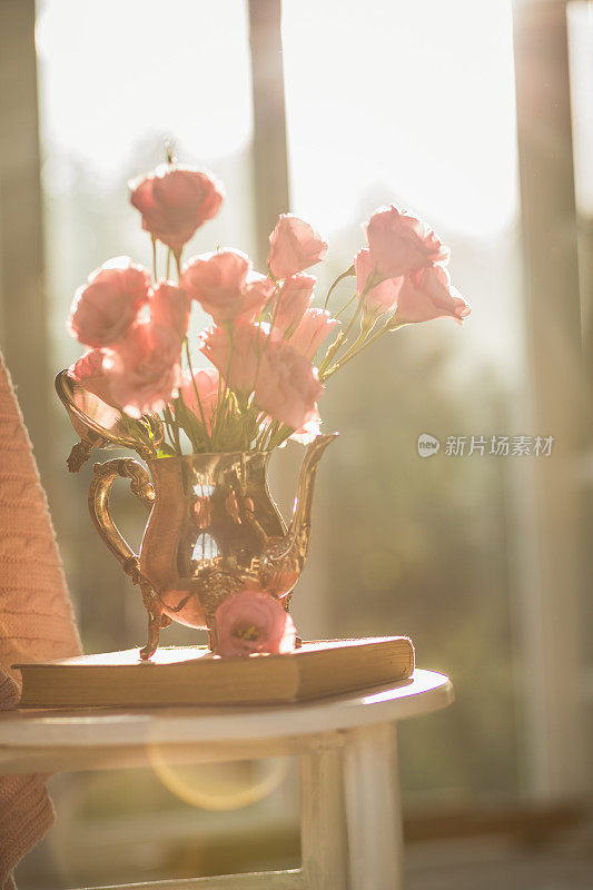 在阳光的照射下，复古的金属花瓶里放着一束粉红色的洋桔黄色花
