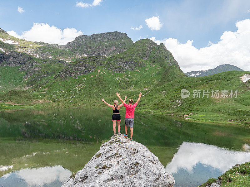 两个徒步旅行者在高山湖的岩石上伸开双臂