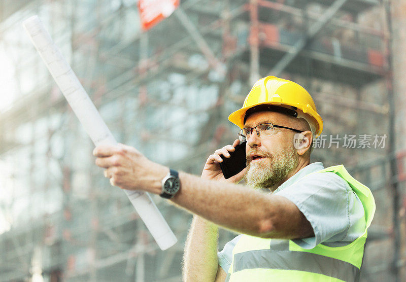 自信的建筑师、土木工程师或建筑承包商在施工现场打着手势，用手机交谈