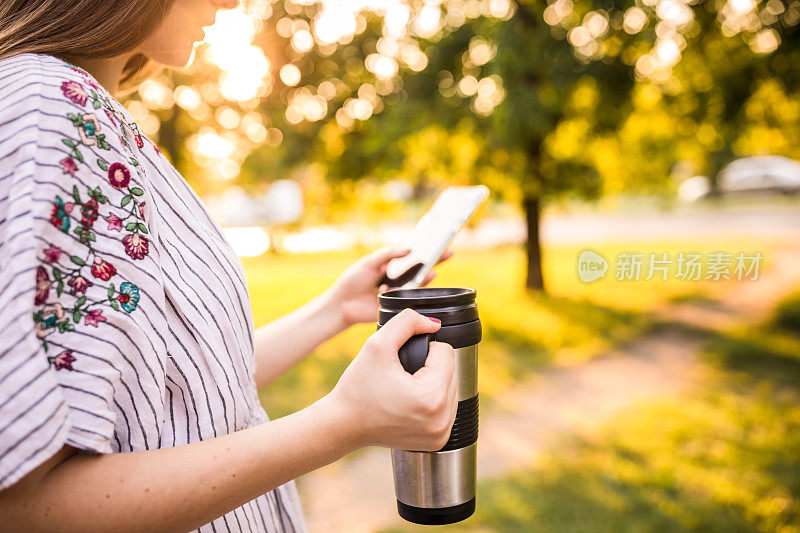 用可重复使用的杯子喝咖啡，给朋友发短信的女人