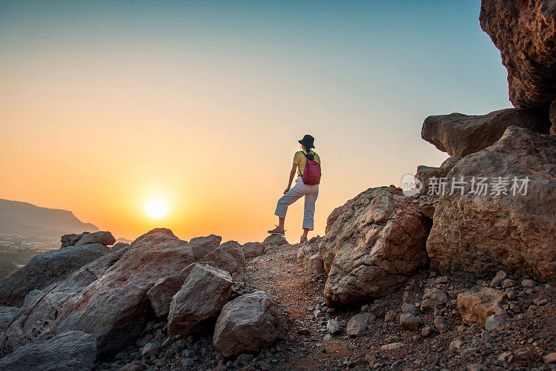 在日落时分的阿联酋沙漠山，一名女子欣赏山顶的景色