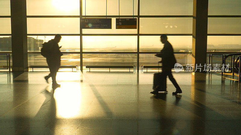 剪影:金色的阳光照耀着穿过机场航站楼的通勤者。