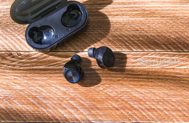 无线耳机或蓝牙耳机与存储和充电盒放在木桌上。本空间