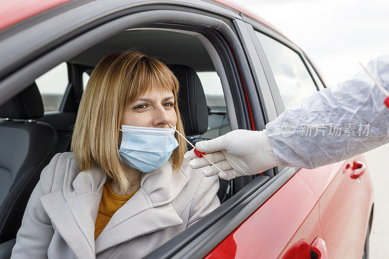 坐在车里的妇女，戴着防护口罩接受医生的鼻拭子检查