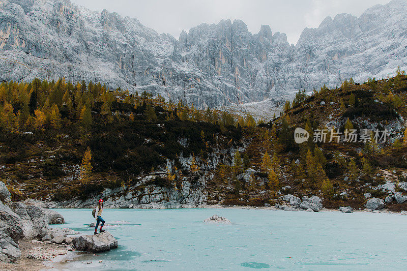 女旅行者呆在岩石上，欣赏阿尔卑斯山上冰封的高山湖泊的风景