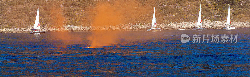 蓝色海洋中的橙色烟雾弹。背景帆船