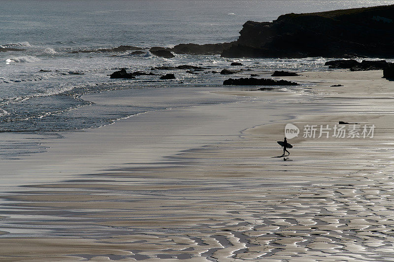 落潮时，一个人带着冲浪板在空荡荡的沙滩上向水走去