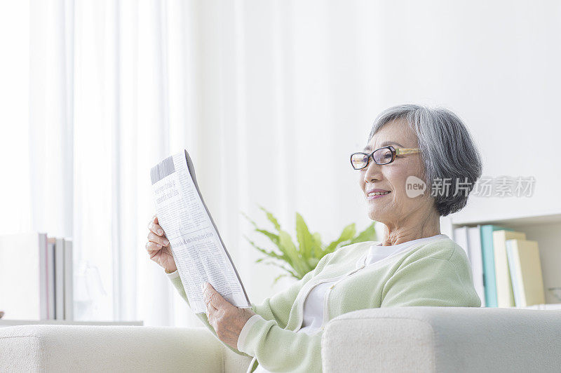 老年女人坐在沙发上看报纸