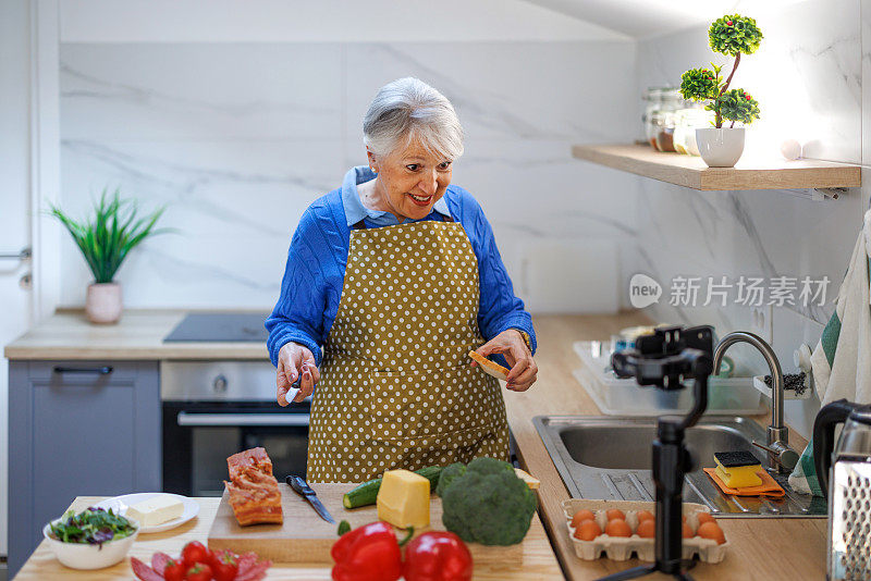 年长妇女准备食物配方，同时在线流与移动智能手机摄像头为网络厨房大师班频道