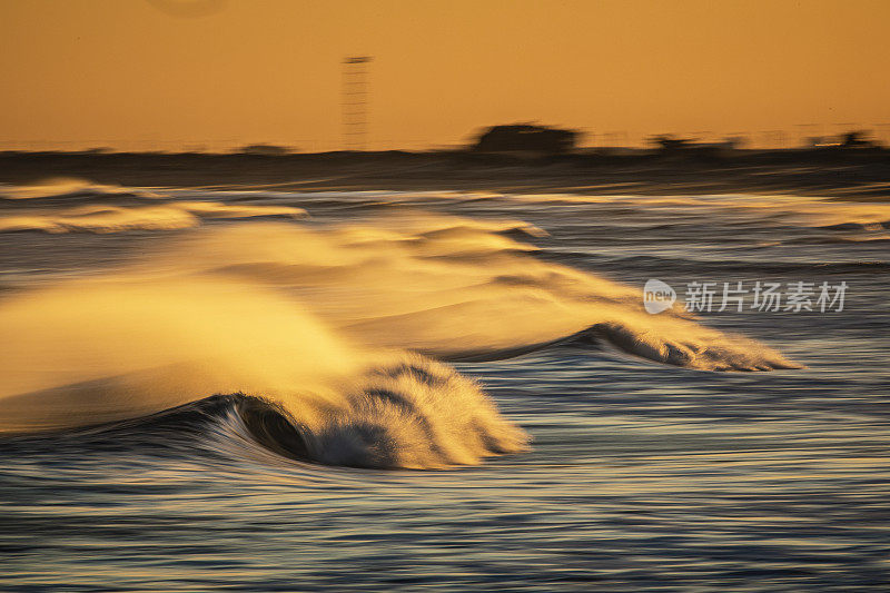 海浪的海景，强风浪花反射出海滩上明亮的金色日出