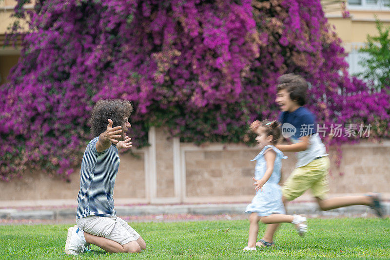 儿子和女儿在公园里奔向父亲的照片