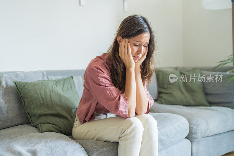 悲伤的年轻女子坐在客厅的沙发上