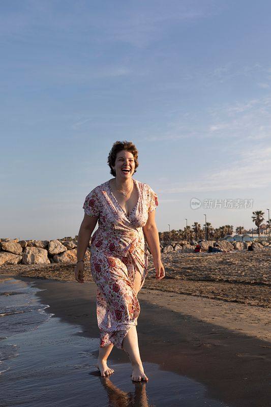 垂直拍摄一个曲线优美的白人女性在日落时走在海滩上