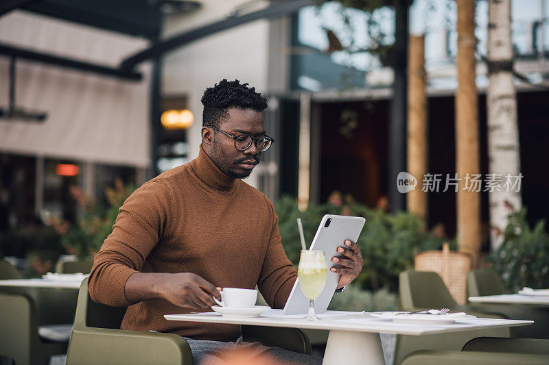 年轻的黑人商人一边用平板电脑一边喝咖啡