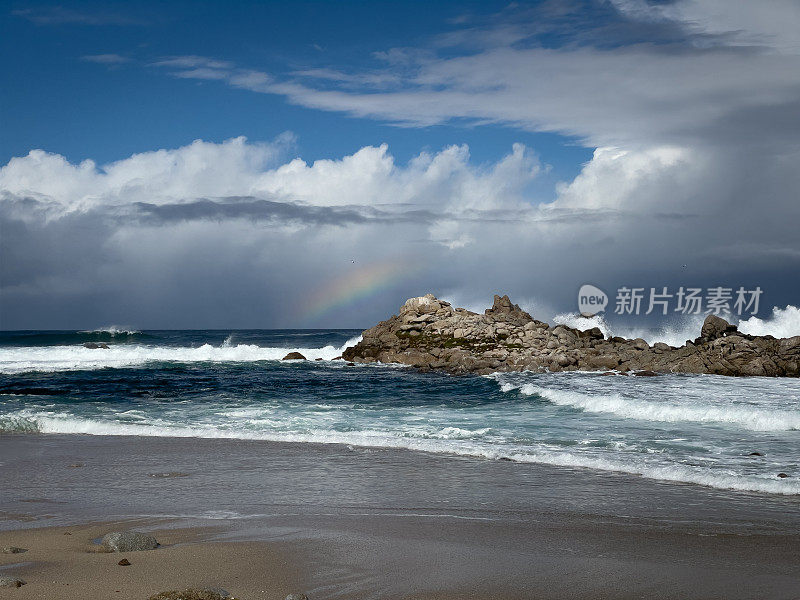 地平线上的彩虹，天空中的暴风雨云，海浪在加利福尼亚蒙特雷县的海滩上撞击岩石