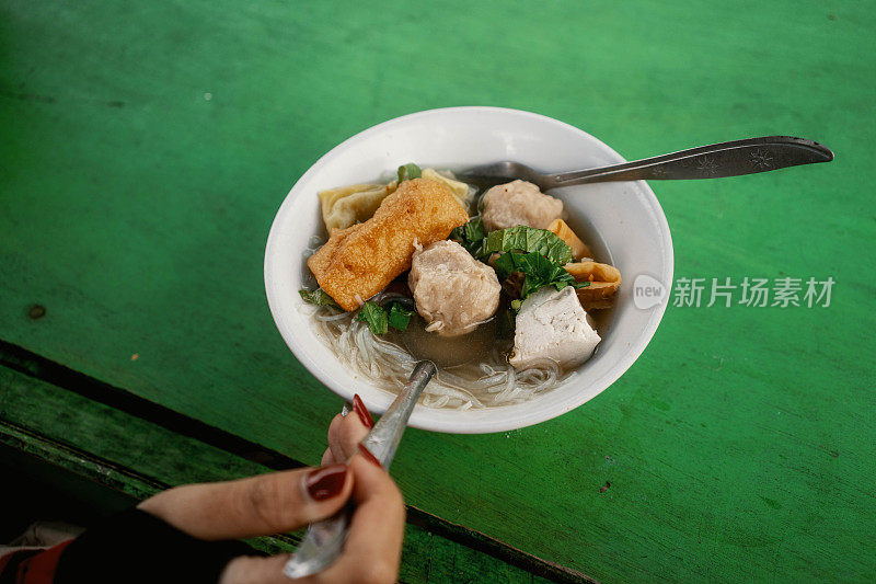 绿色木桌上的传统食品——女手拿器巴索肉丸特写