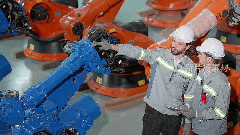 团队工业工程师，穿着安全制服，在自动化生产的机械臂工厂工作，在机械臂生产线检查后维护的实用系统或在制造工厂测试操作。产业创新