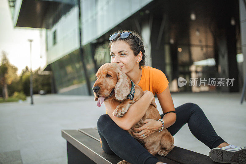 年轻女子和她的可卡犬坐在城市的长凳上